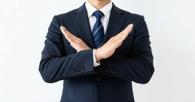 スーツを着た営業マンが胸元でバツのジェスチャーをしている