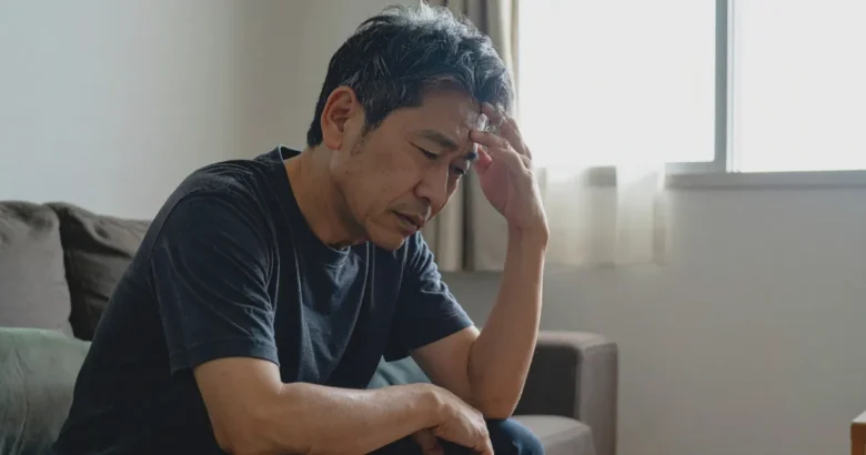 リビングでソファに座っている男性が、俯きながら頭を抱えている