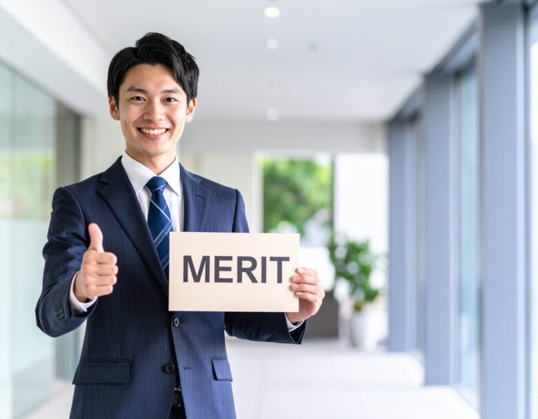 スーツを着た日本人男性が笑顔で手を親指をたててグッドとしている。もう片方の手には「メリット」と書かれたパネルを持っている。
