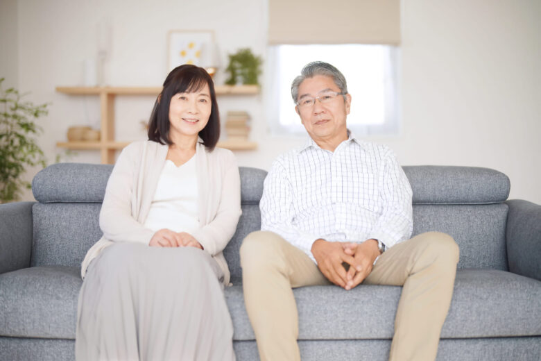家のソファーに50～60代の夫婦が座っているのを正面から撮った写真