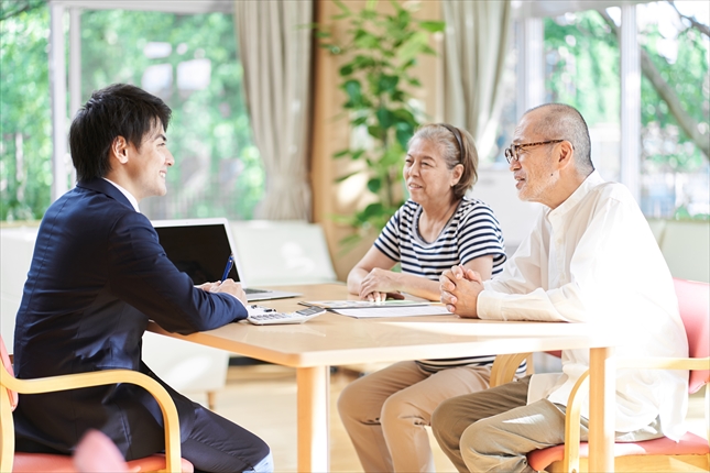 家の中で相談中の老夫婦とビジネスパーソン。老夫婦とビジネスパーソンは向き合う形で椅子に座っている。笑顔で話していて和やかな雰囲気