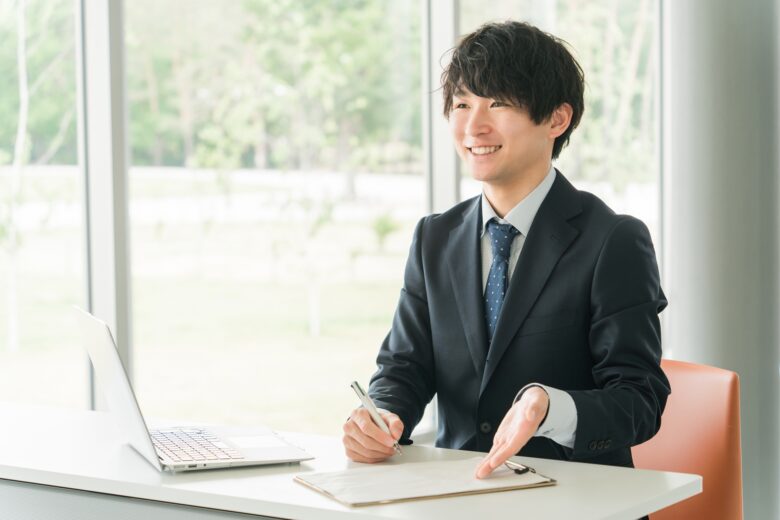 ビジネスマンが机の上にある資料を指しながら、笑顔で説明している様子。