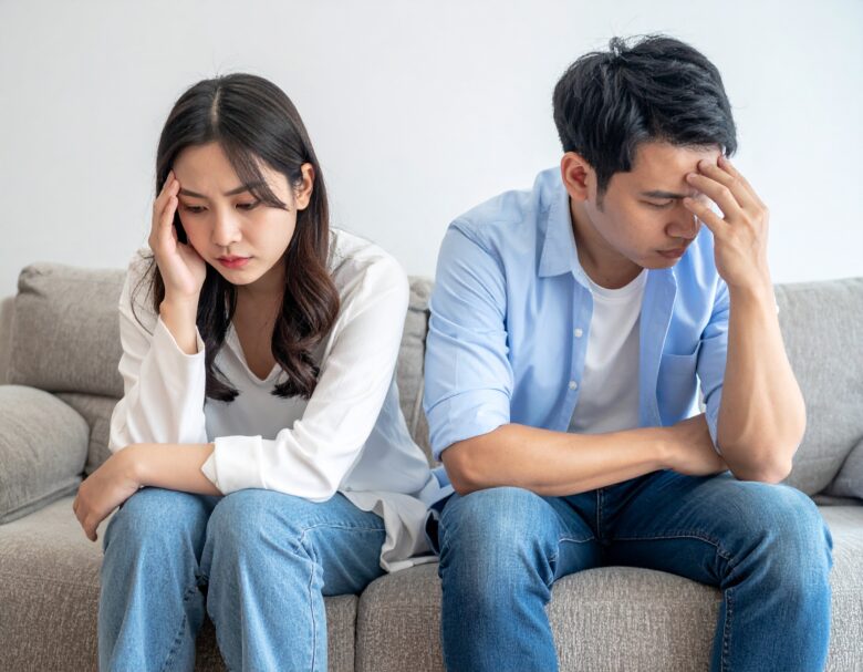 日本人夫婦がソファに座って頭を抱えている。