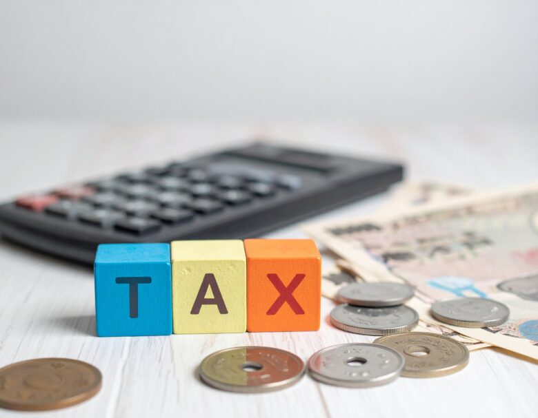 TAXと書かれたカラフルなブロックと電卓とお金が置いてある