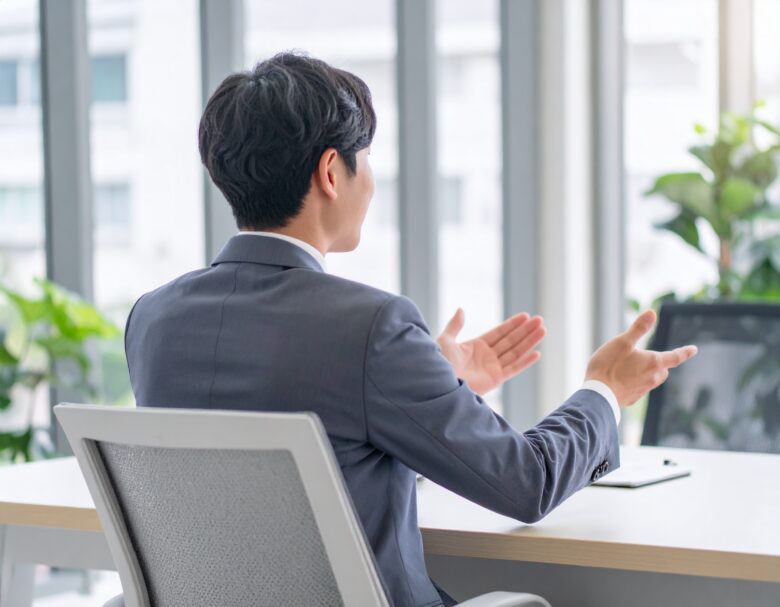 身振り手振りを交えて話す、スーツを着た男性の後ろ姿