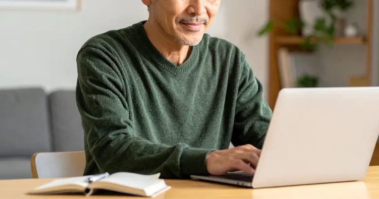 男性がリビングでパソコンを使って調べ物をしている。机の上にはメモとペンが置かれている。