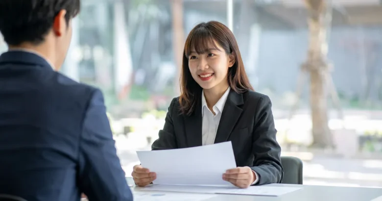 スーツを着た女性が、机の上の資料について説明している